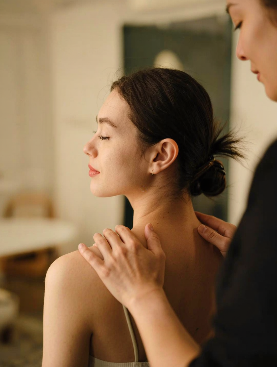 Therapist's hands offering light support over a client's shoulders and upper back